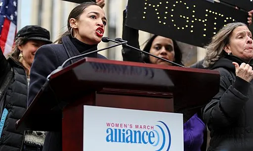 Alexandria Ocasio-Cortez speaking behind a podium @ Women's March NYC, 2019