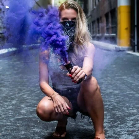 woman bending on concrete pavement holding blue smoke